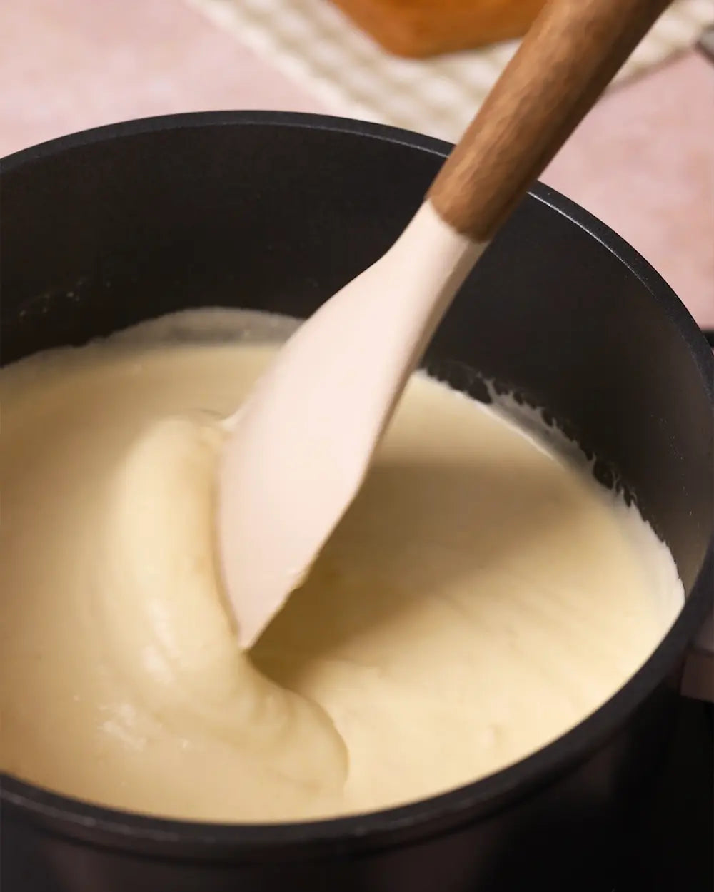 Black pot with creamy pasta sauce and a wooden spoon stirring it.