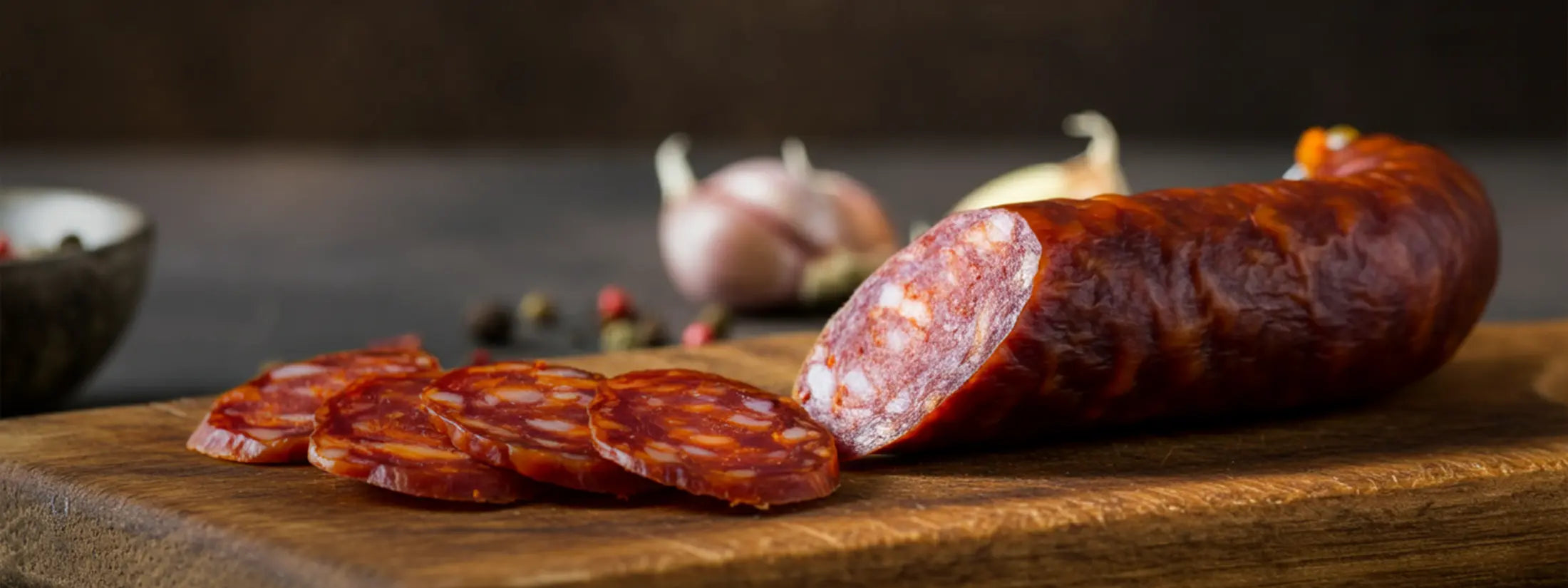 Sliced and whole chorizo Spanish sausages on a wooden cutting board with garlic and peppers.