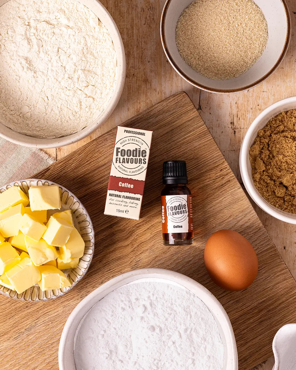 Baking ingredients including flour, butter, an egg, and a bottle of Foodie Flavours coffee flavouring on a wooden surface.