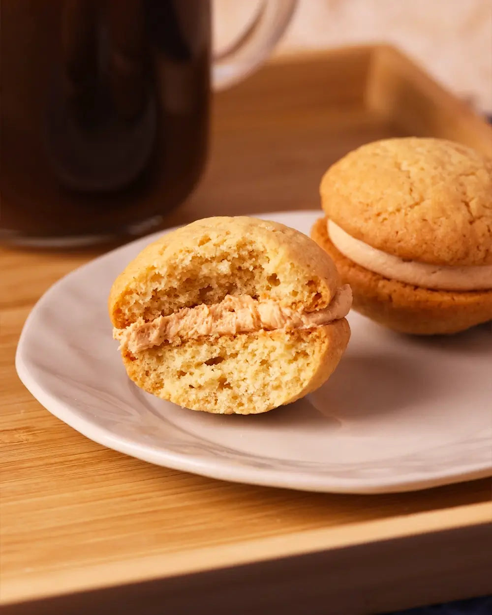 Two coffee kisses on a white plate with a cup of coffee in the background.