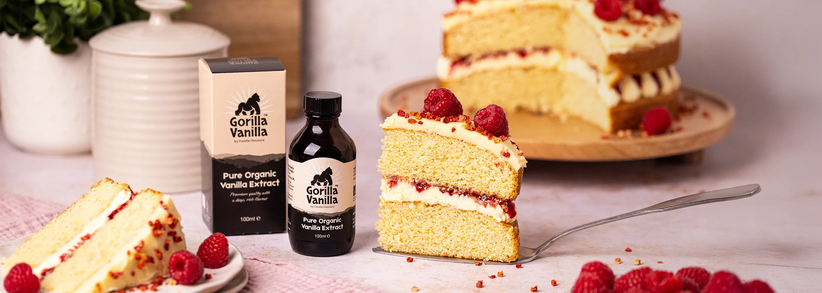Bottle of Gorilla Vanilla vanilla extract with packaging on a surface with cakes and raspberries.