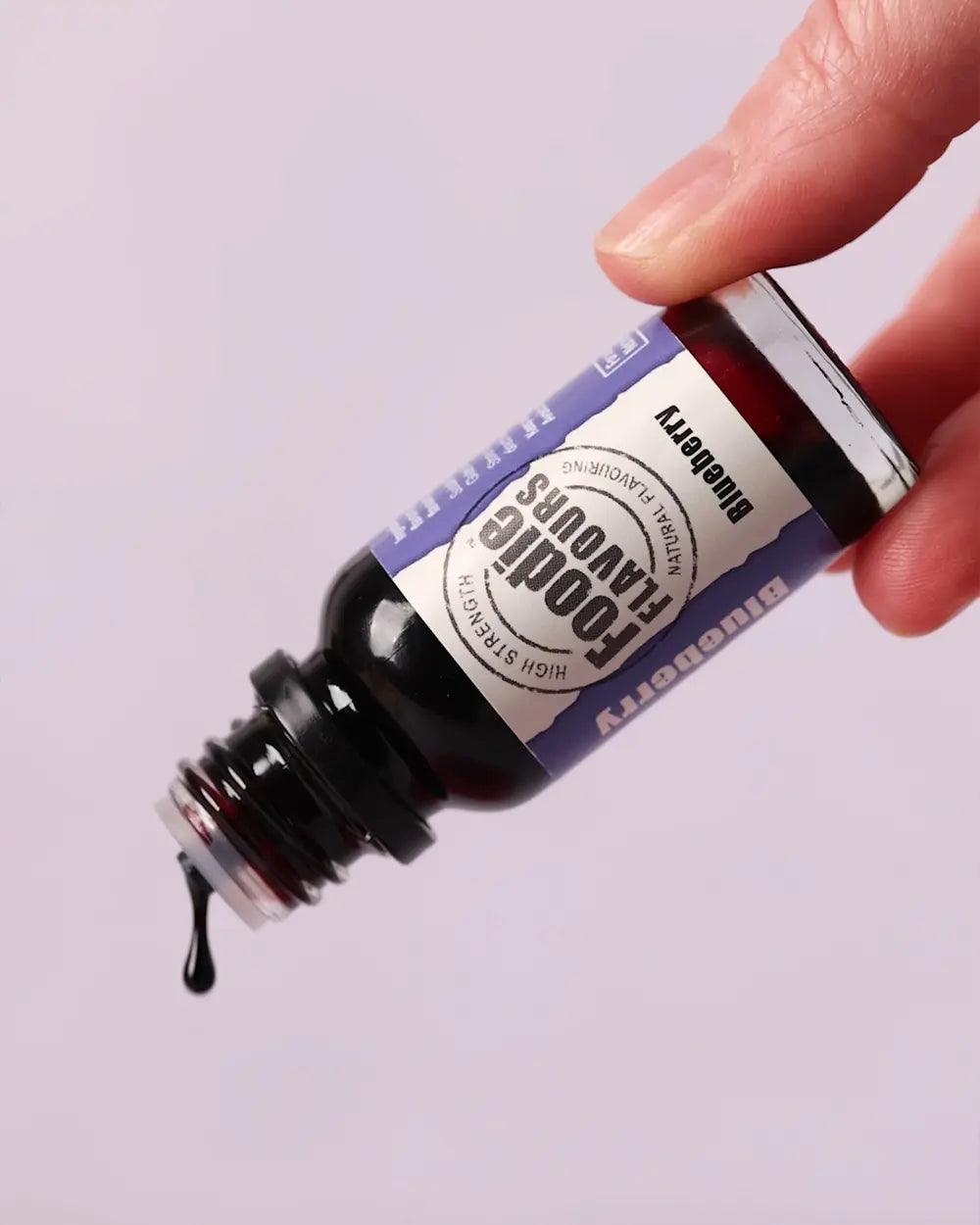 Glass bottle of foodie flavours' blueberry natural flavouring being used, drops of flavour are dripping out of the inverted end