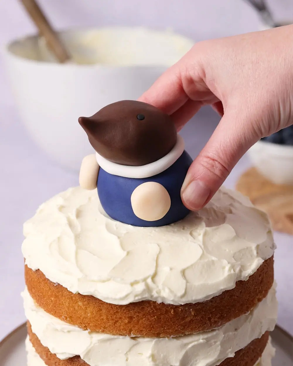 a fondant mole figure being added to a layered sponge cake