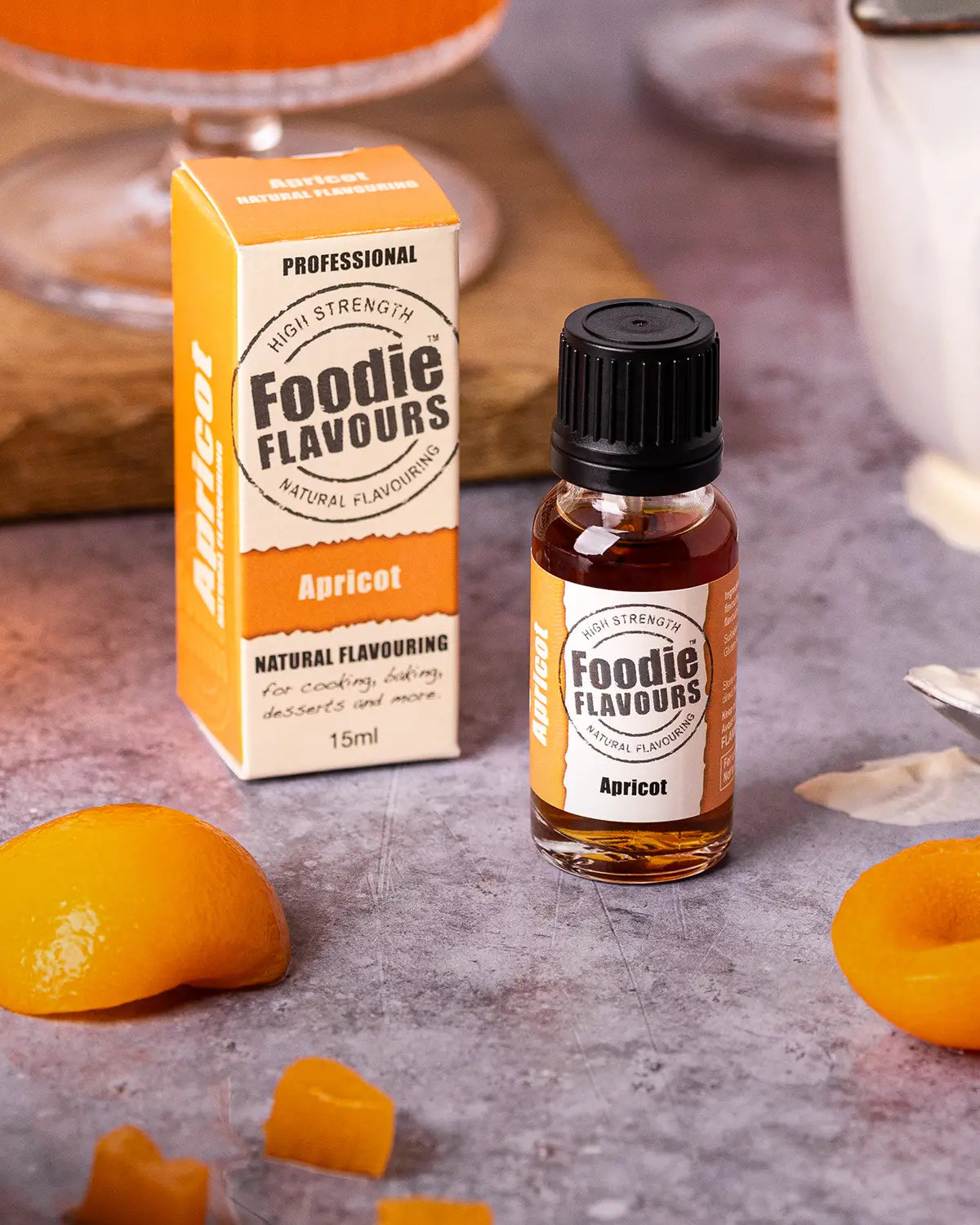 Glass bottle of Foodie Flavours Natural Apricot Food Flavouring, surrounded by slices of apricot and apricot flavoured jelly in dessert glasses.