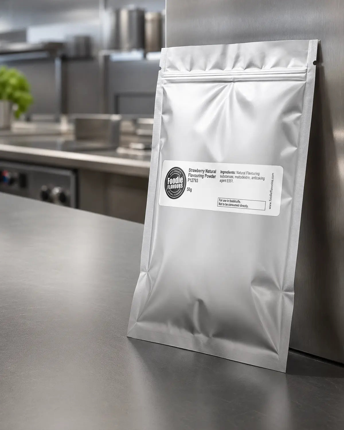 Silver foil sachet of strawberry natural flavouring powder on a metallic surface with a label in a catering kitchen setting
