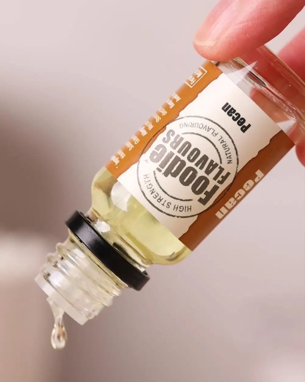 Bottle of pecan food flavouring with a dropper, held by a hand against a neutral background
