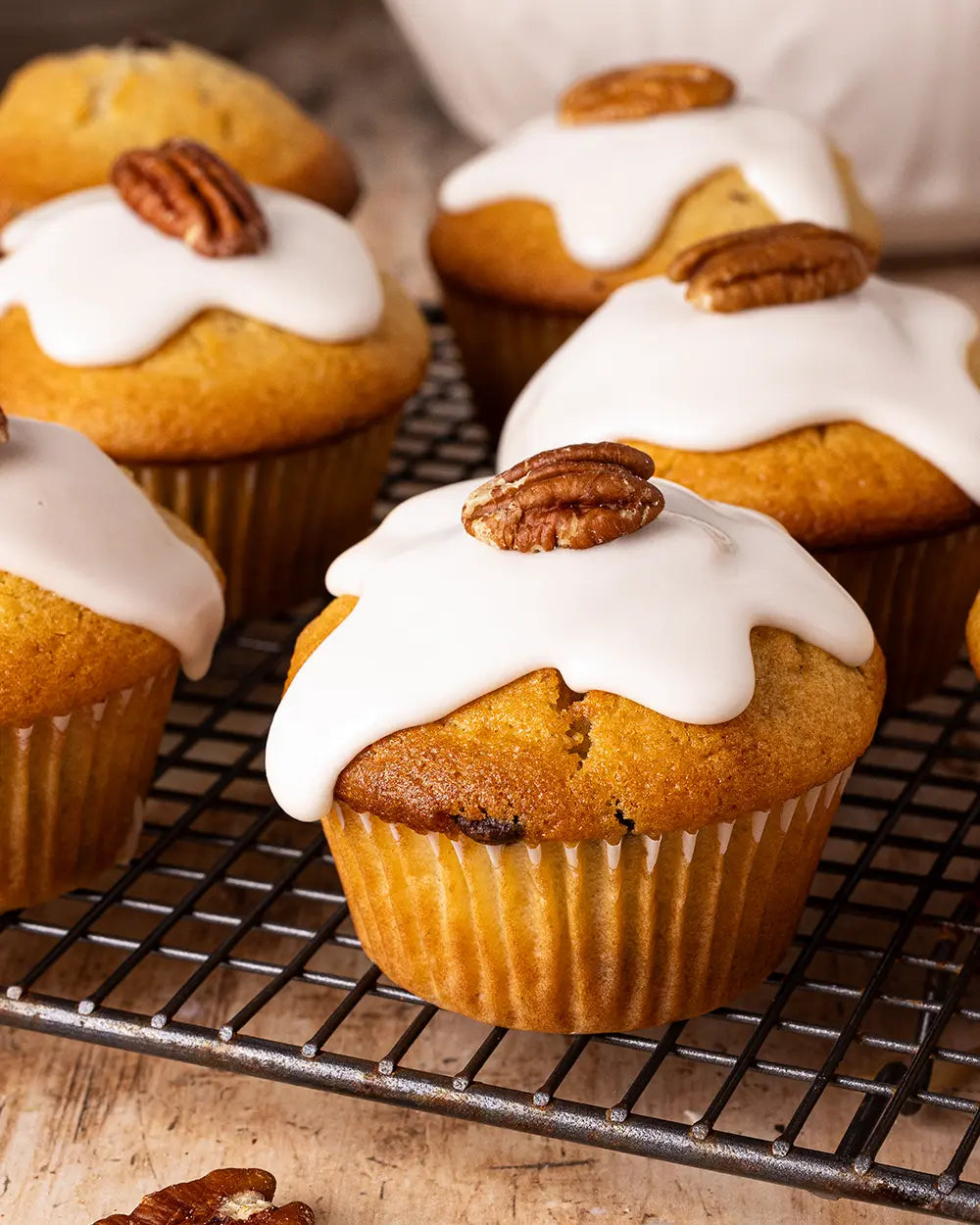 Pecan muffins with white icing and topped with pecans on a cooling rack.