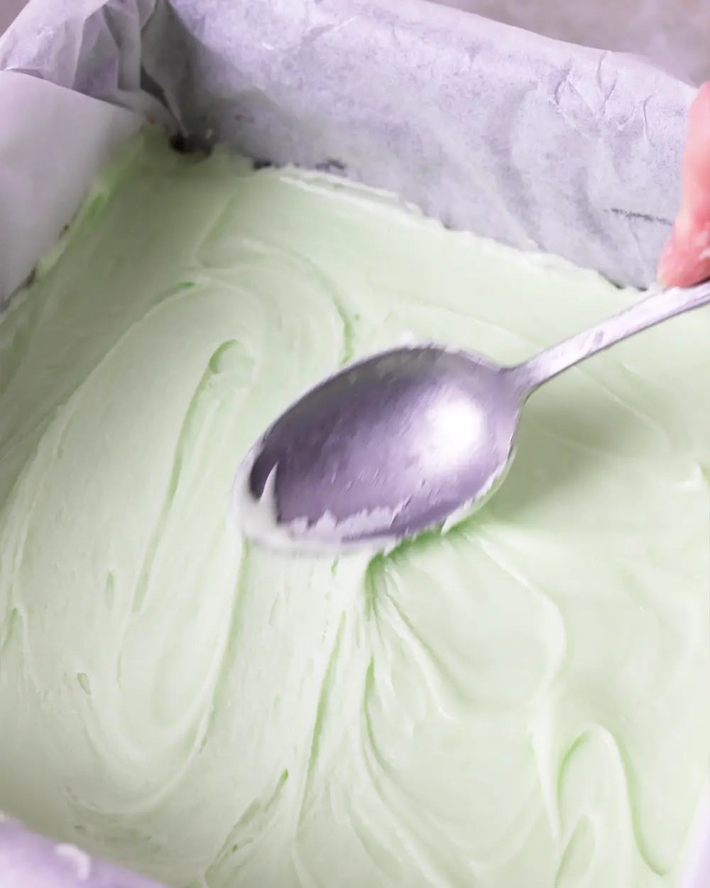 Green peppermint icing spread with a spoon in a baking dish.