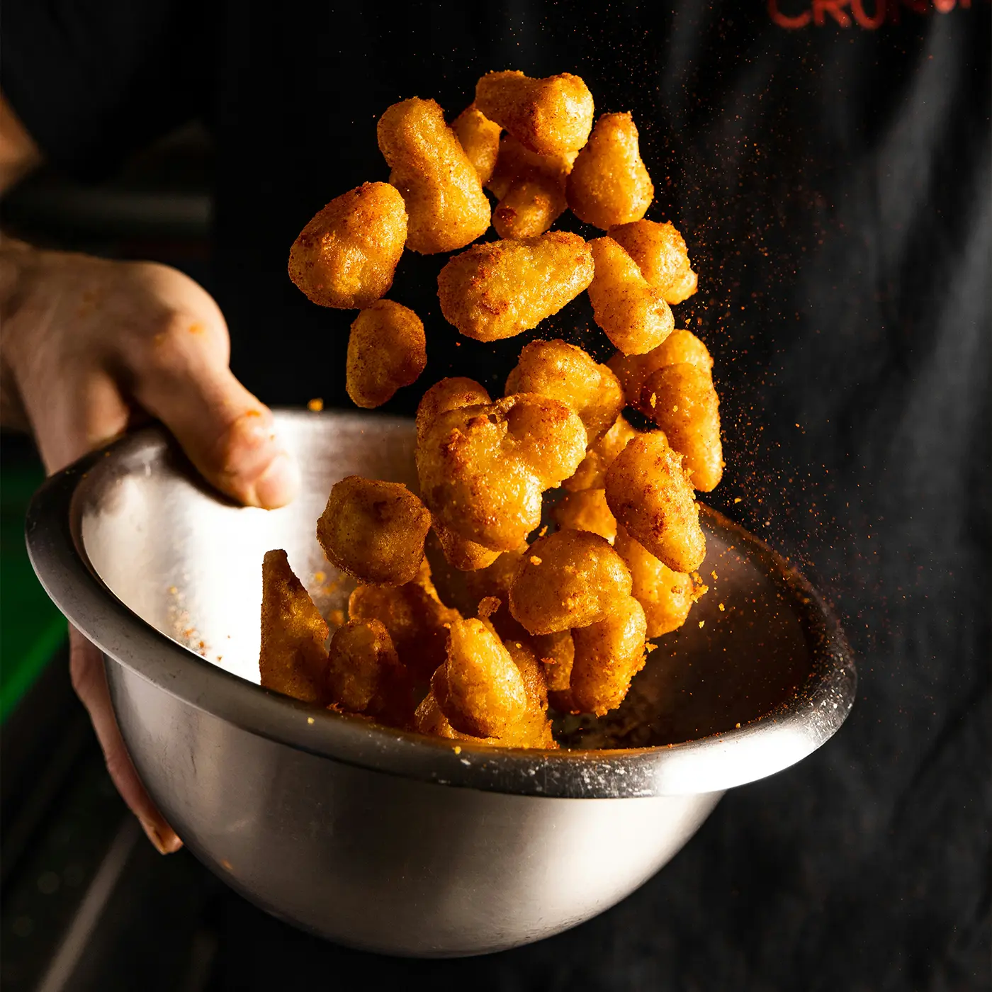 Metal bowl filled with golden-brown fried cauliflower being tossed in a chicken flavoured seasoning