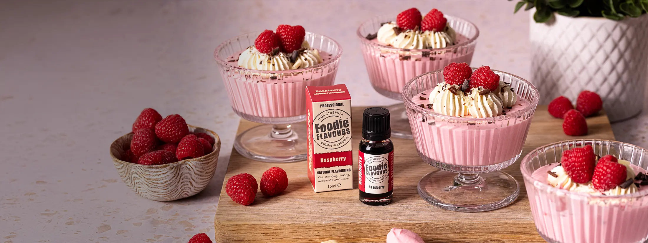 Bottle of raspberry food flavouring, raspberry flavoured pink coloured mousse in dessert glasses topped with cream and raspberries