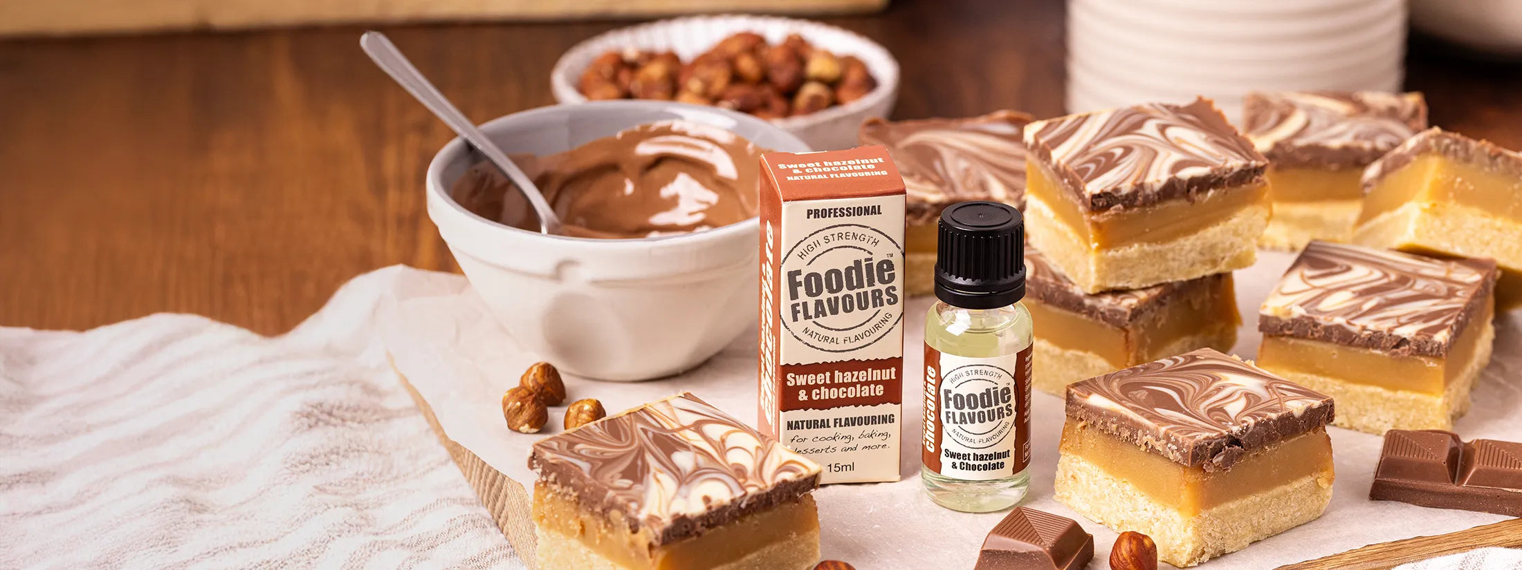 Hazelnut Millionaire's Shortbread squares Fudge on a wooden board with a bottle of Foodie Flavours Sweet Hazelnut & Chocolate Natural Flavouring.