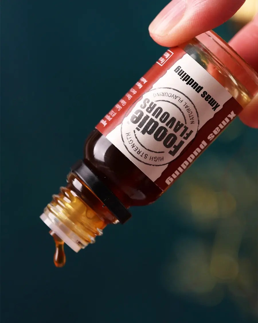 Bottle of foodie flavours xmas pudding flavouring, held inverted with a single drop coming out the dropper