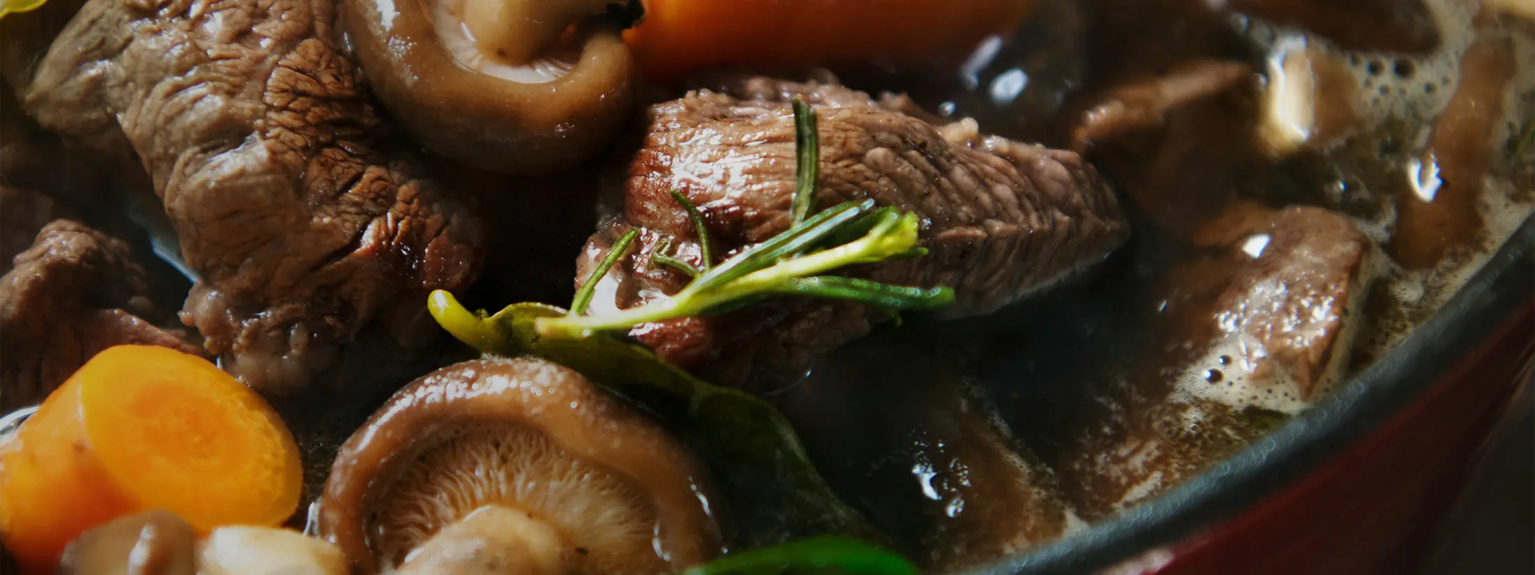 Close-up of a bowl of beef and mushroom stew with carrots and herbs.