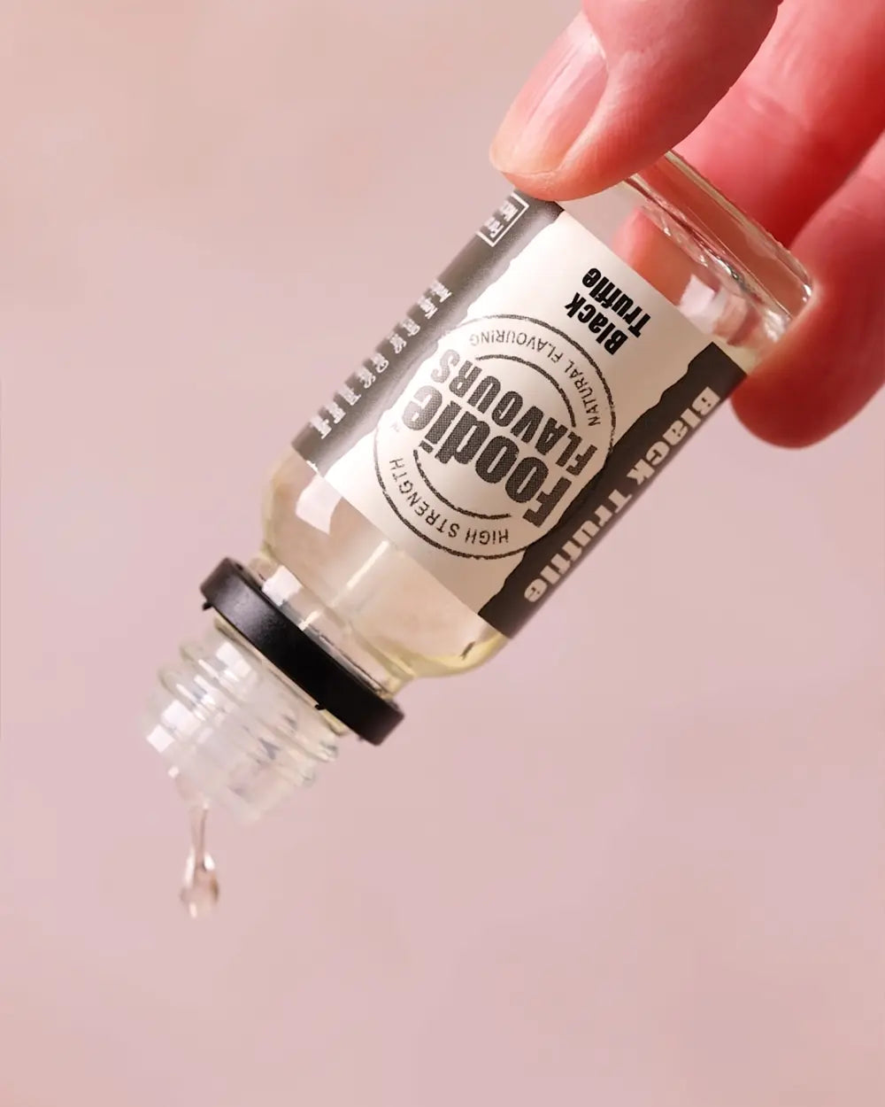 Bottle of black truffle food flavouring with a dropper on a pink background