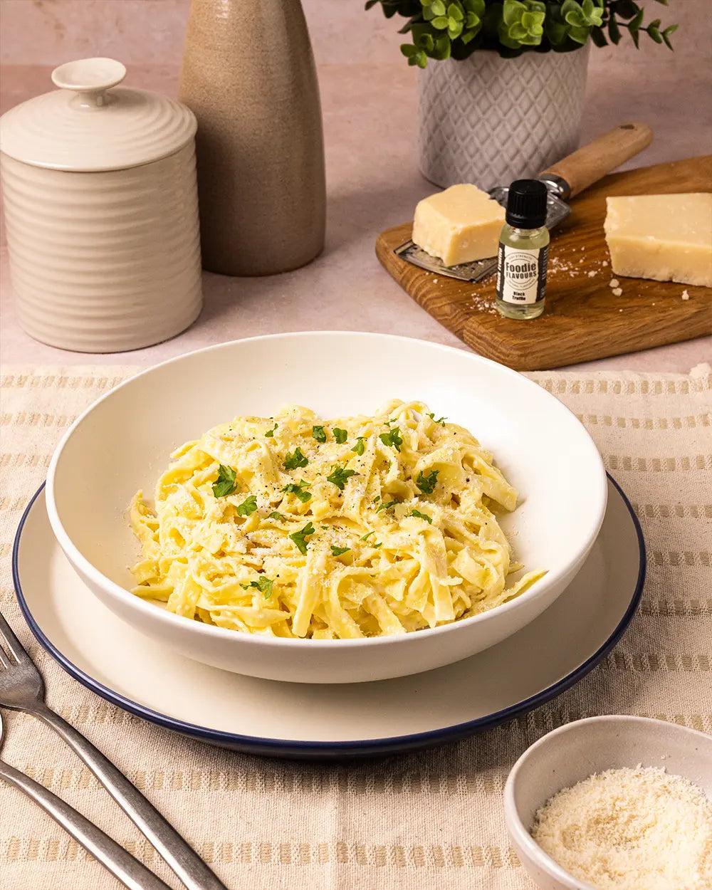 Bowl of tagliatelle pasta in a black truffle infused sauce, in the background is a glass bottle of Foodie Flavours Black Truffle Natural Flavouring