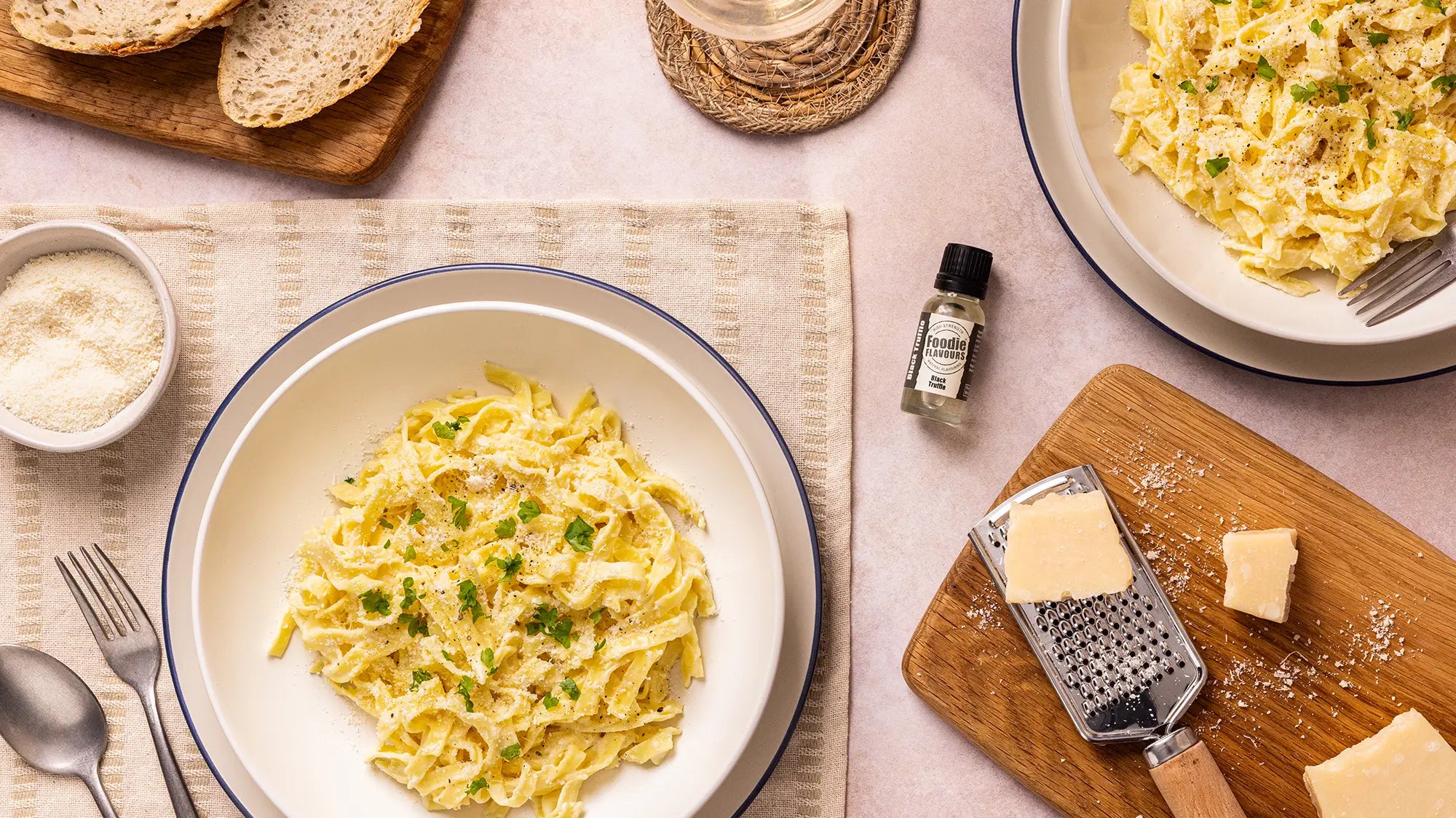 Bowl of tagliatelle pasta in a black truffle infused sauce, in the background is a glass bottle of Foodie Flavours Black Truffle Natural Flavouring