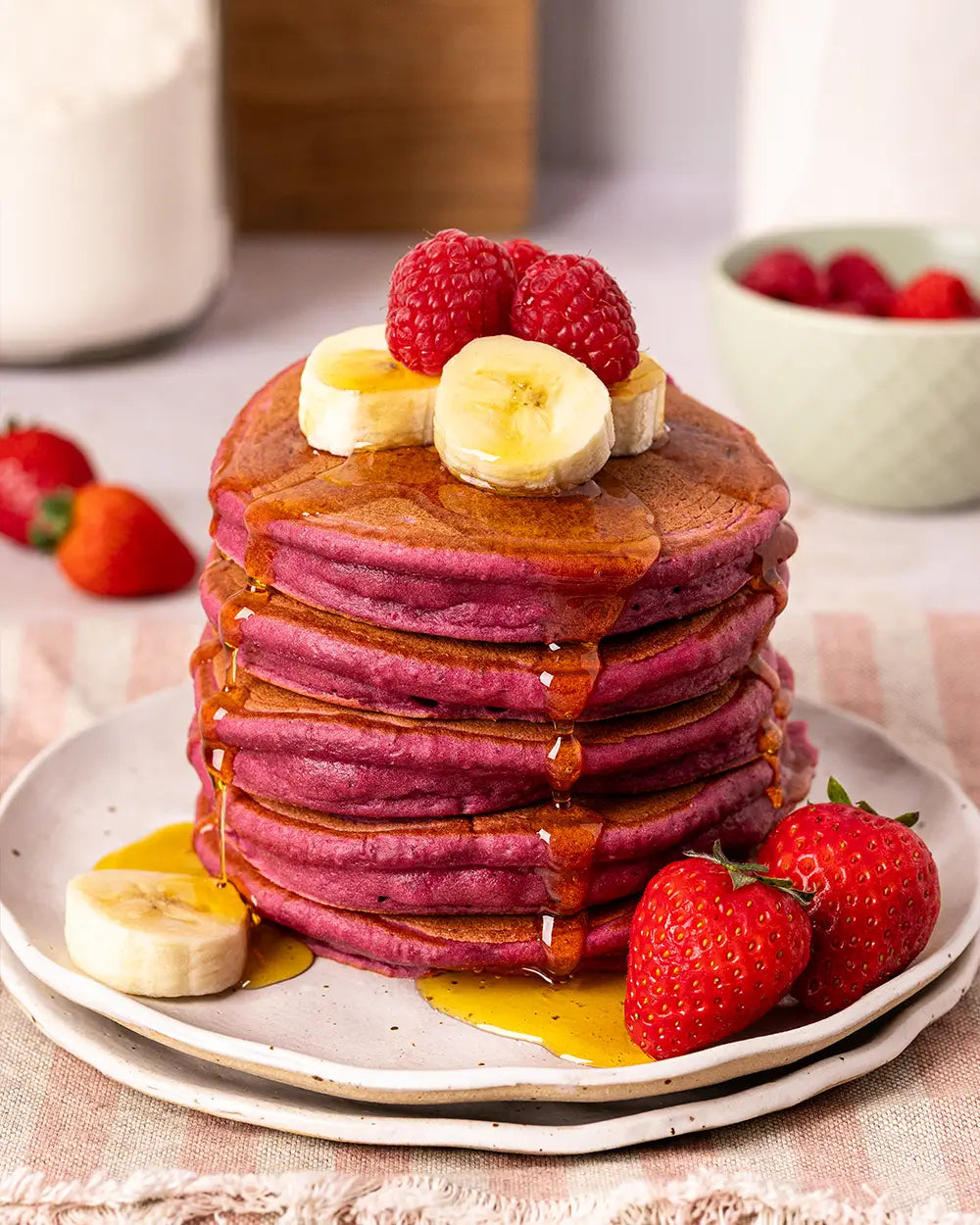 Stack of blackcurrant flavoured pink pancakes with fruit on a white plate