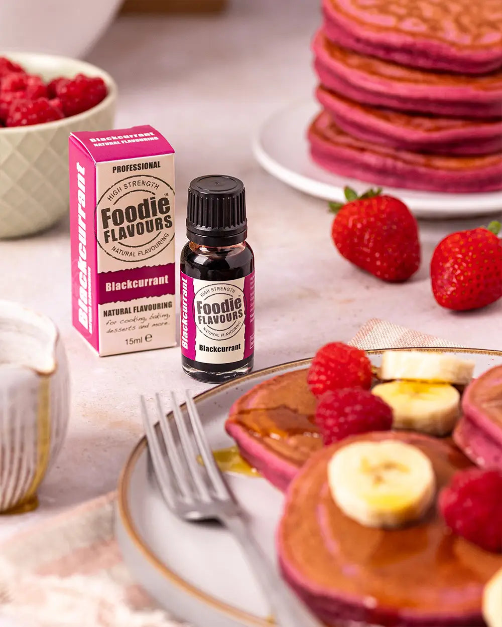 Bottle of Foodie Flavours blackcurrant flavouring with a stack of pancakes and berries on a table.