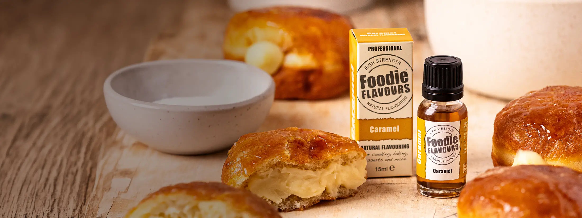 A bottle of Foodie Flavours caramel natural flavourings and its matching box, styled on a wooden surface with caramel doughnuts