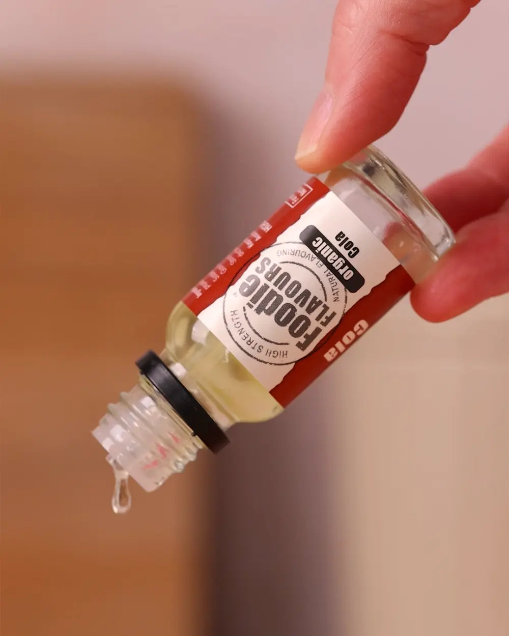 Inverted glass bottle of foodie flavours organic cola flavourings, drops are coming out.
