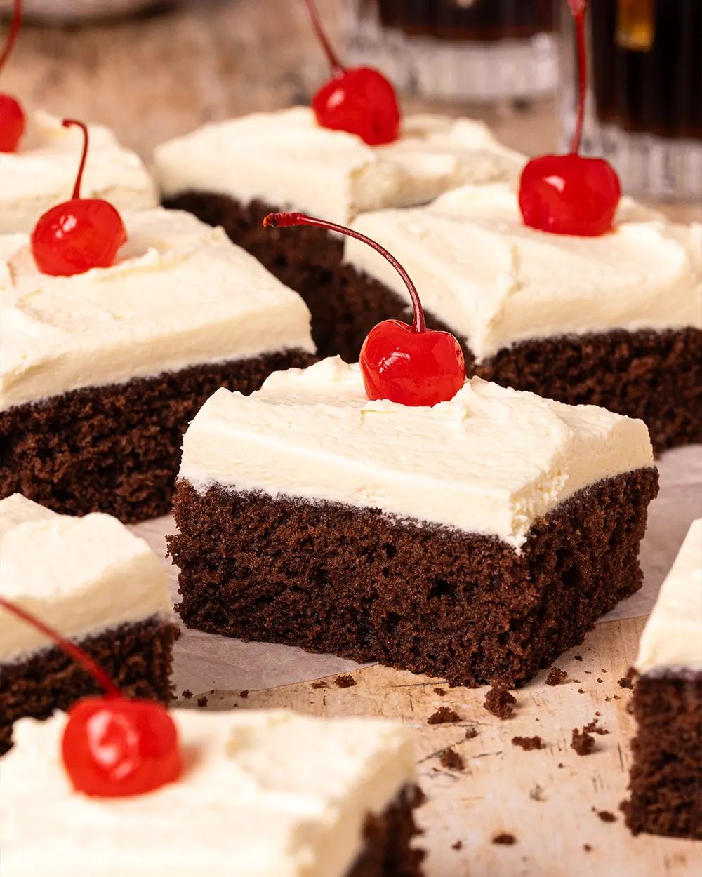 Chocolate traybake cake with white vanilla cream topping and cherries on a wooden surface