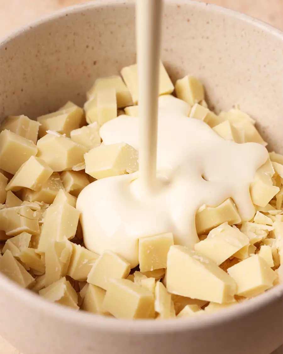 cream being poured into a bowl full of white chocolate pieces.