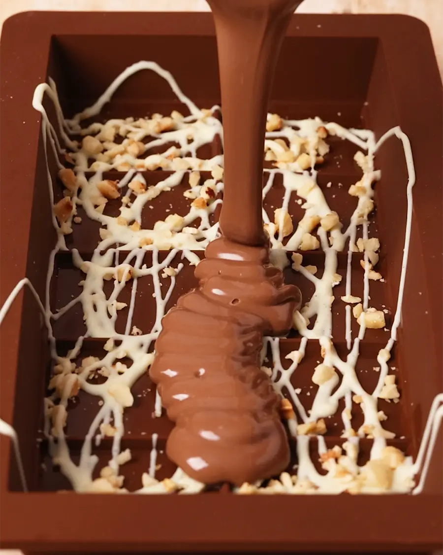 Chocolate being poured into a mould with nuts and white chocolate drizzle.