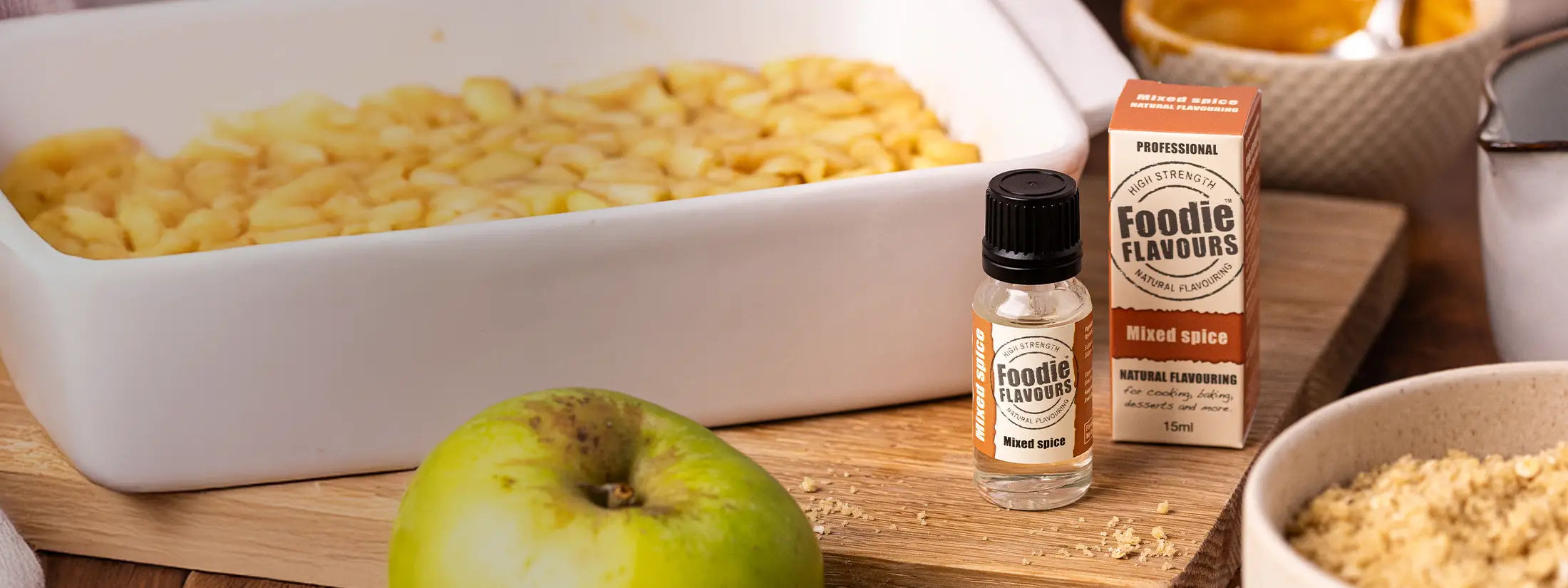 Bottle of Mixed Spice food flavouring on wooden chopping board with dish of apple crumble