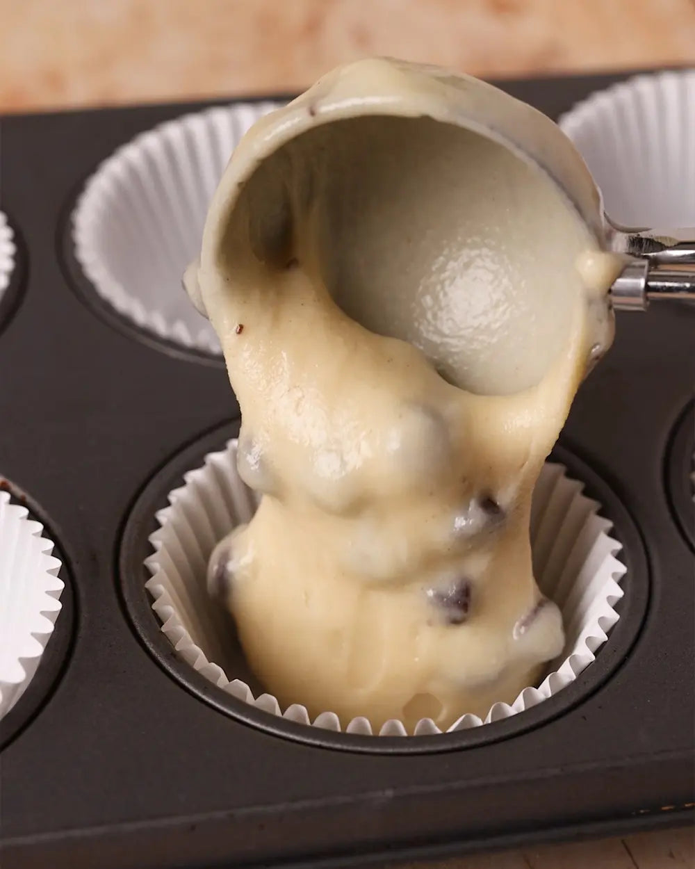Muffin tin with a cupcake liner and a scoop of batter being added.
