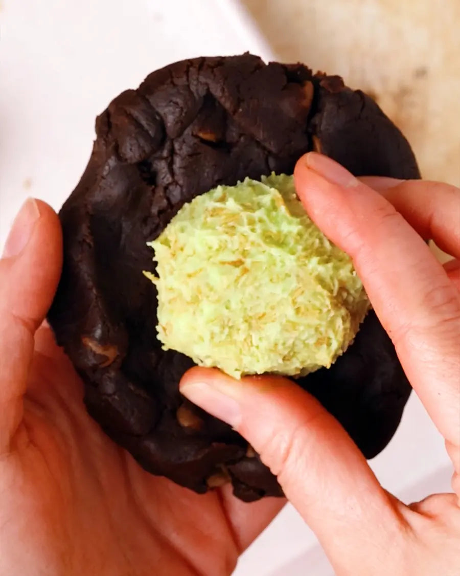 Chocolate cookie with a green ball of Dubai chocolate filling being held by hands