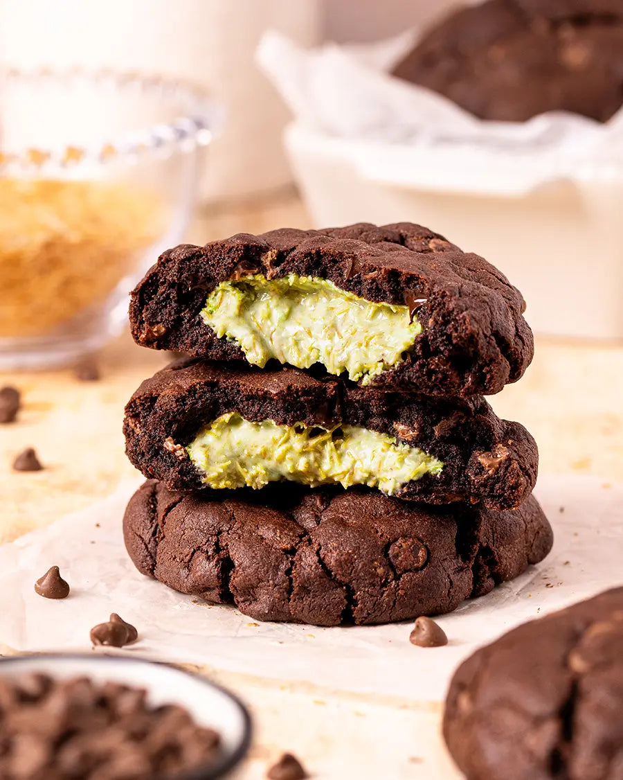 Stack of chocolate cookies with green Dubai chocolate filling on a wooden surface