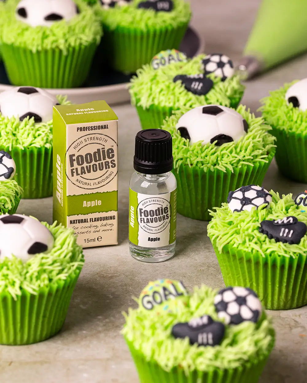 Glass bottle of foodie flavours apple essence, apple flavoured football themed cupcakes with bright green piped grass